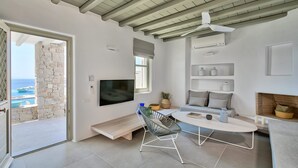 Ein modernes Wohnzimmer mit Fernseher, Sitzgelegenheiten und Meerblick.