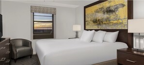 Ein Hotelzimmer mit einem großen Bett, einem Sessel, einem Schreibtisch, einer Lampe, einem Gemälde und einem Fenster mit Blick.