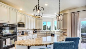 A kitchen with white cabinetry, a granite countertop island, and blue upholstered chairs. - Ridgemont Hall! Grand Mountain Home w/ Peak Views (Monument)