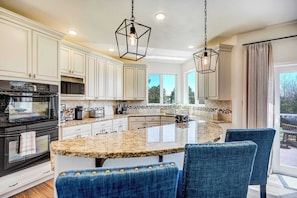 A kitchen with white cabinetry, a granite countertop island, and blue upholstered chairs.