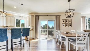 A modern kitchen with a central island, white cabinetry, and a dining area with a wooden table and chairs. - Ridgemont Hall! Grand Mountain Home w/ Peak Views (Monument)