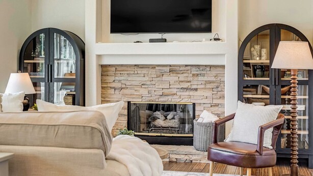 A living room with a fireplace, a sofa, a chair, and a TV mounted above the fireplace. - Ridgemont Hall! Grand Mountain Home w/ Peak Views (Monument)