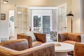 A room with a large sliding glass door leading to a balcony, leather sofas, a round coffee table, and a floor lamp.