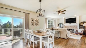 A spacious living room with a wooden floor, a dining table with white chairs, a sofa, a fireplace, a TV, and a ceiling fan. - Ridgemont Hall! Grand Mountain Home w/ Peak Views (Monument)