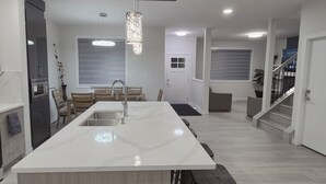 A modern kitchen with a large island, built-in appliances, and a staircase leading to another level. - Vibrant Homestead (Edmonton)
