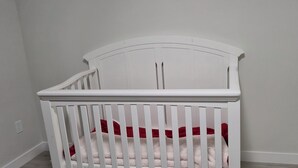 A white crib with a curved headboard, positioned against a plain wall with a visible electrical outlet. - Vibrant Homestead (Edmonton)