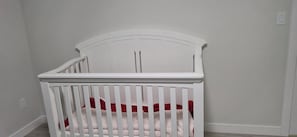 A white crib with a curved headboard, positioned against a plain wall with a visible electrical outlet. - Vibrant Homestead (Edmonton)