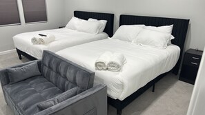 Habitación de hotel con dos camas, un sillón tapizado en gris y una mesita de noche.