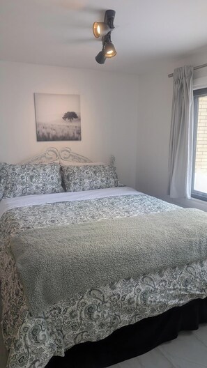 Une chambre à coucher avec un lit, un luminaire au plafond, une fenêtre avec des rideaux et un tableau accroché au mur.