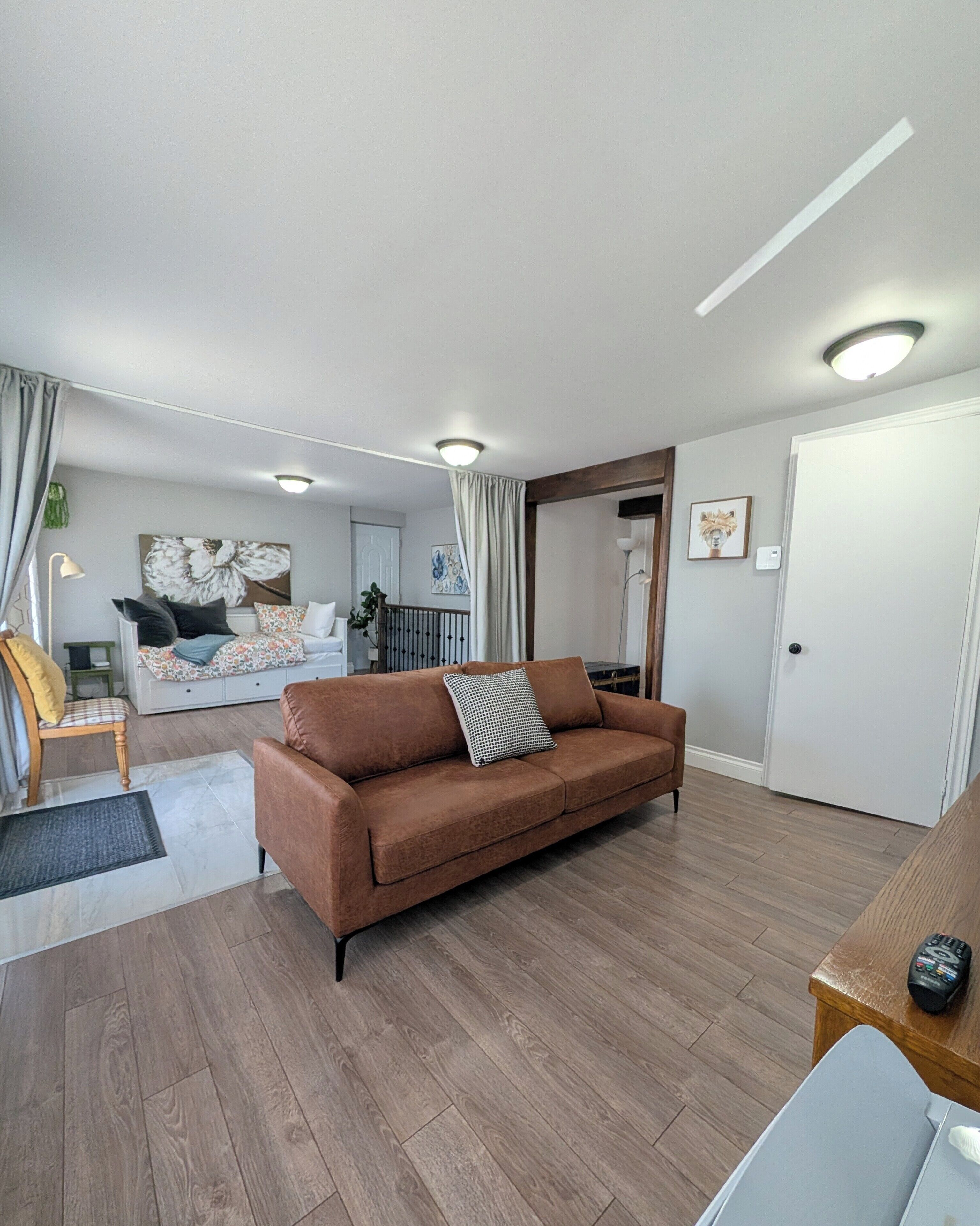 Un salon avec un canapé marron, un plancher en bois et une porte blanche.