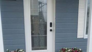 A front door with a number '5684' above it, two potted plants, and a floral mat on the concrete porch.