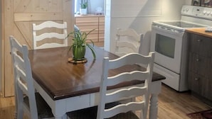 Un coin repas avec une table en bois et des chaises blanches, une cuisine équipée d’une cuisinière et de placards, et une porte en bois.