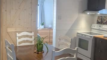 A dining area with a wooden table and white chairs, a kitchen with a stove and cabinets, and a wooden door.