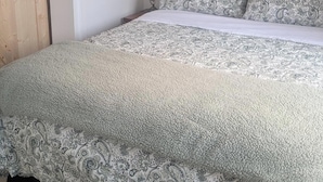 Une chambre à coucher comprenant un lit, une table de chevet, une lampe fixée au mur, un thermostat et un tableau encadré accroché au mur.