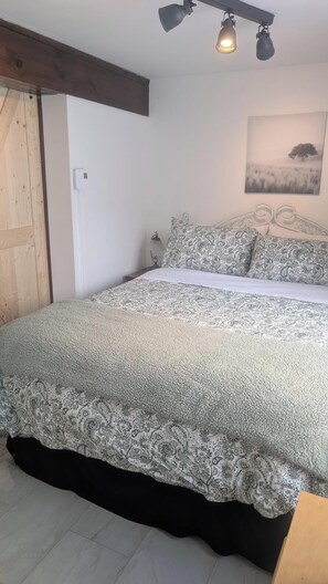 A bedroom with a bed, a nightstand, a wall-mounted lamp, a thermostat, and a framed picture on the wall. - In the heart of old Lévis! Close to the ferry that will take you to Old Quebec! (Lévis)