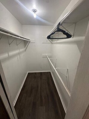 Ein schmaler begehbarer Kleiderschrank mit weißen Wänden, Holzboden und einer Deckenleuchte.