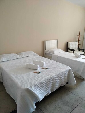 Een hotelkamer met twee bedden, elk voorzien van witte lakens en kussens, een stoel en een houten kapstok.
