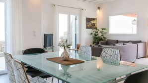 A modern living room with a glass dining table, a sofa, and a TV. - Kalafatis Stay With Private Pool (Mykonos)