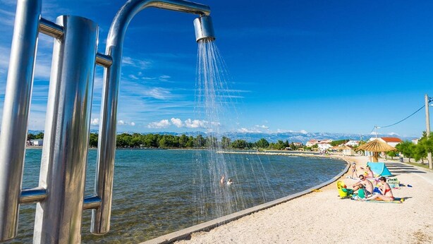 Una estructura metálica de donde brota agua, una playa arenosa y un cielo azul despejado.