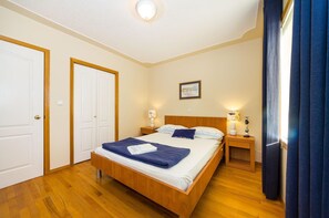 Quarto com cama de madeira, duas mesas de cabeceira com luminárias, um quadro na parede e uma porta.