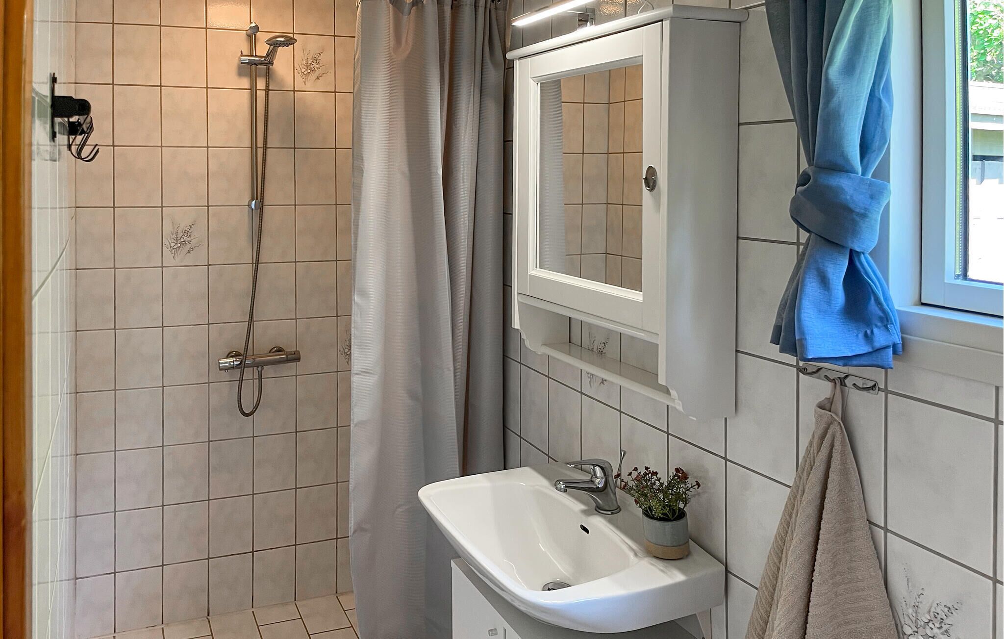 Een badkamer met een douche, wastafel, spiegel en handdoekrek.