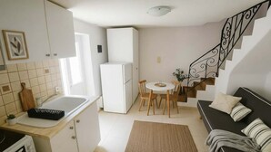 A compact kitchen with a refrigerator, a dining table with chairs, a sofa, and a staircase.