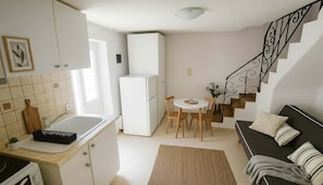 A compact kitchen with a refrigerator, a dining table with chairs, a sofa, and a staircase. - Lefkes Home With Village Views (Paros)