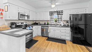 Una cocina moderna con armarios blancos, electrodomésticos de acero inoxidable, un refrigerador negro y una ventana con cortinas a cuadros.