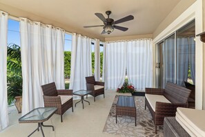 A covered patio area with wicker furniture, a ceiling fan, and a view of greenery outside.