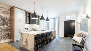 A modern kitchen with a marble island, pendant lights, and a black door. - Rare Yorkville Detached House with Parking and Hot Tub (Toronto)