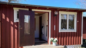 Eine rote Holzhütte mit Holztür, einem Fenster und einer kleinen Veranda mit Stufen.