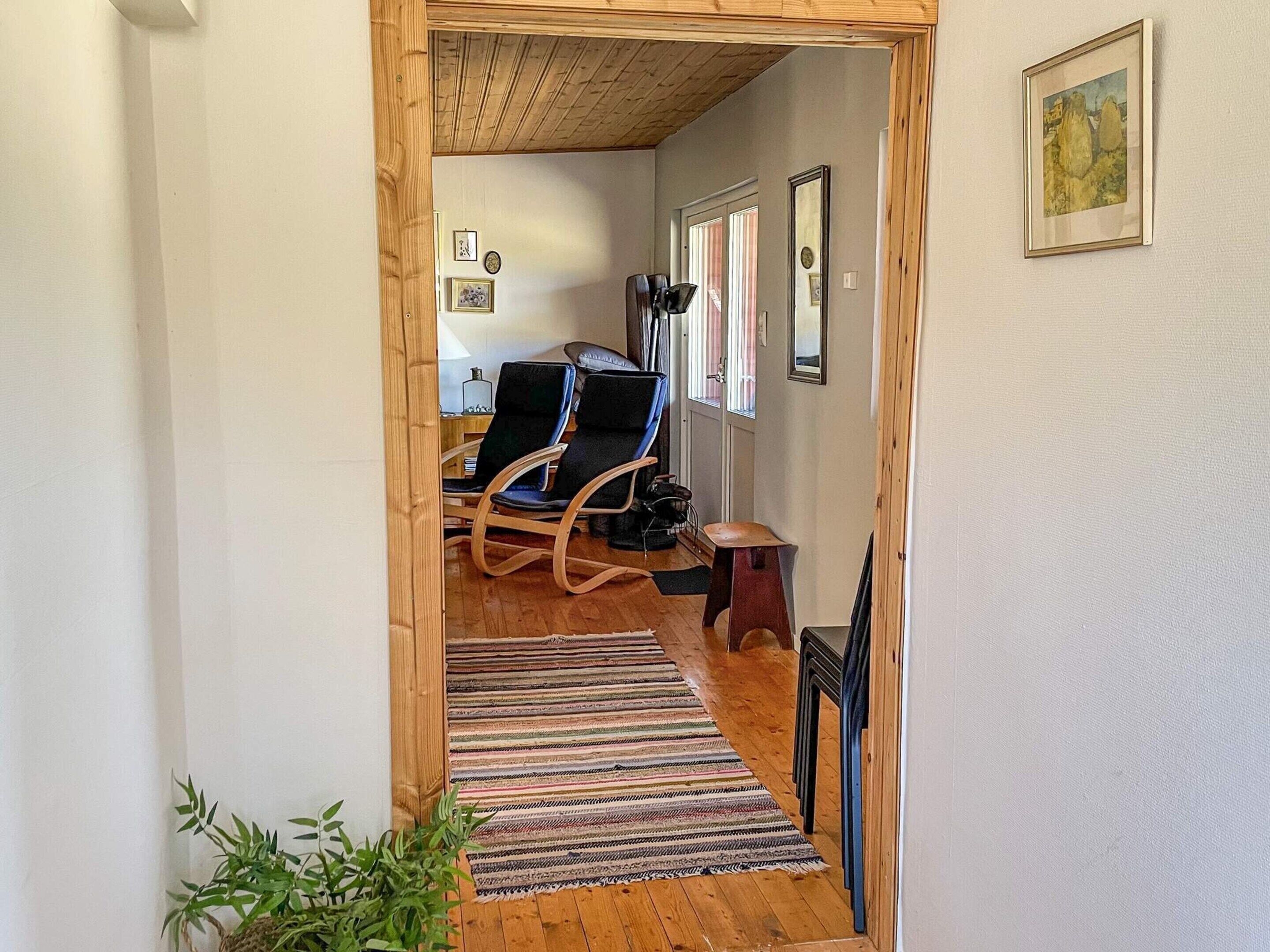 A hallway leading to a room with a wooden ceiling, a black chair, a small stool, and a striped rug.