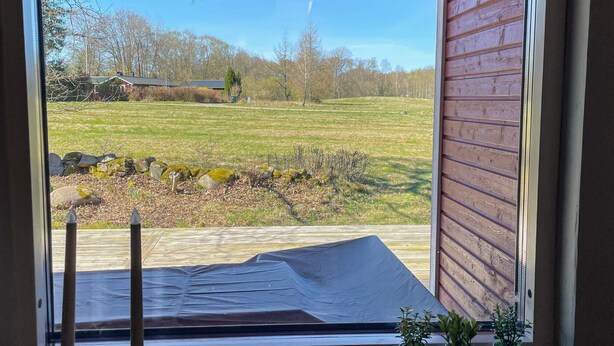 Ein Fenster mit Blick auf ein Wiesfeld, eine Steinmauer und ein Holzgebäude im Hintergrund.
