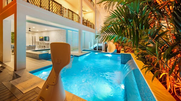 An indoor swimming pool with a wooden deck, a seating area with chairs, and a staircase leading to an upper level. - Direct Beach Access, Panoramic Rooftop, Pool/Spa (Clearwater)