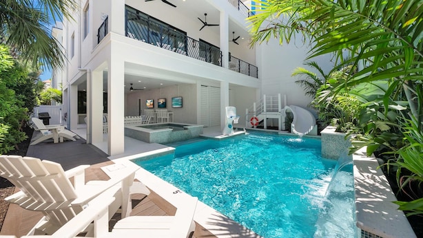 A modern pool area with a slide, lounge chairs, and a two-story building with balconies. - Direct Beach Access, Panoramic Rooftop, Pool/Spa (Clearwater)