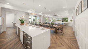 A modern kitchen with a large island, dining area with wooden chairs, and a view of the outdoors. - Direct Beach Access, Panoramic Rooftop, Pool/Spa (Clearwater)