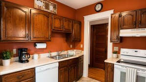 A kitchen with wooden cabinets, a dishwasher, a stove, and a clock on the wall.