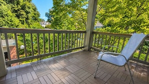 A covered outdoor area with a wooden deck, metal railing, and a single metal chair.