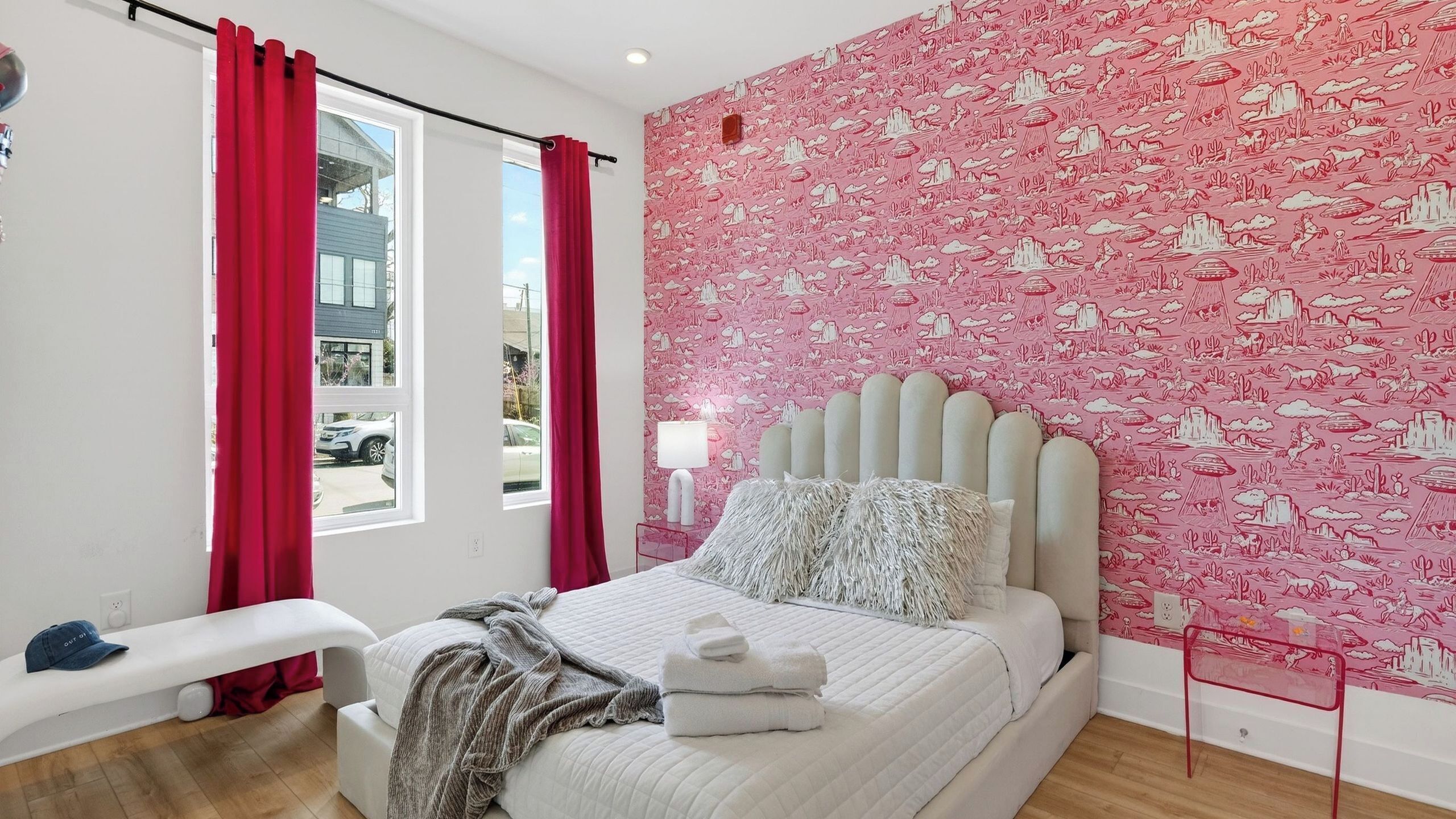 A bedroom with a bed, a bench, a window, and a wall with a pink pattern.