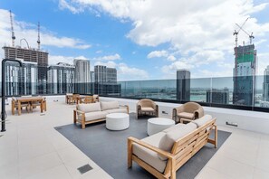 A rooftop lounge with outdoor furniture, a glass balustrade, and a city skyline view. - Modern Downtown Suite | Walk to Bayfront Park (Miami)