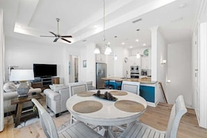 A modern living room with a dining table, sofa, TV, and kitchen area.