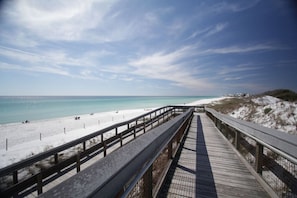 A wooden boardwalk leading to a beach with white sand and clear turquoise water.