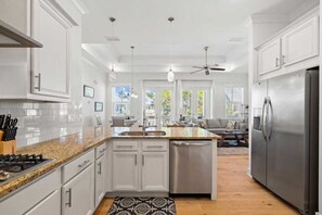 A modern kitchen with white cabinetry, granite countertops, a dishwasher, a refrigerator, and a ceiling fan.