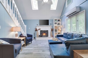 A living room with a fireplace, blue sofas, a TV, and a staircase. - Cozy 4-bedroom chalet in The Hideout pet friendly with AC, hot tub (Cobbs Lake Preserve)