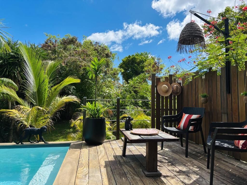 Une terrasse en bois avec une piscine, des espaces de détente en plein air et une végétation luxuriante.