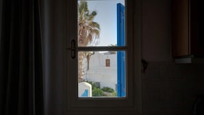 A window with a view of a white building and a palm tree. - Ornos Home With Sea View (Mykonos)