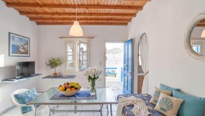 A room with a wooden ceiling, a table with a fruit bowl, a sofa with decorative pillows, and a television on a stand. - Ornos Home With Sea View (Mykonos)