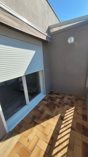 A corner of a building with a closed window, a tiled floor, and a wall with a circular feature. - Apartment T2 Centre Port Cap d'Agde (Agde)