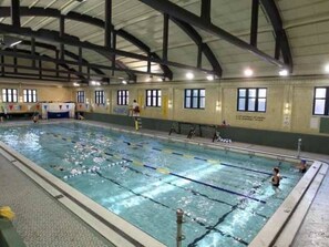Ein Hallenbad mit mehreren Bahnen, hohen Decken und Fenstern an den Wänden.