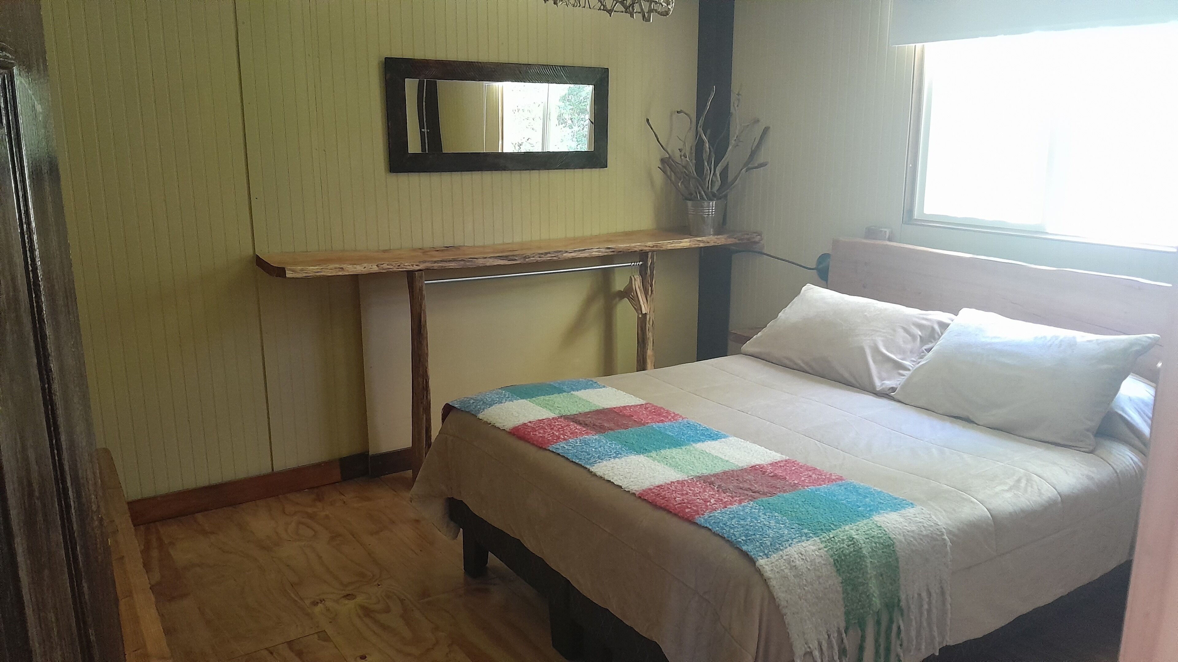 Un dormitorio con cama, mesita de noche, espejo y ventana.